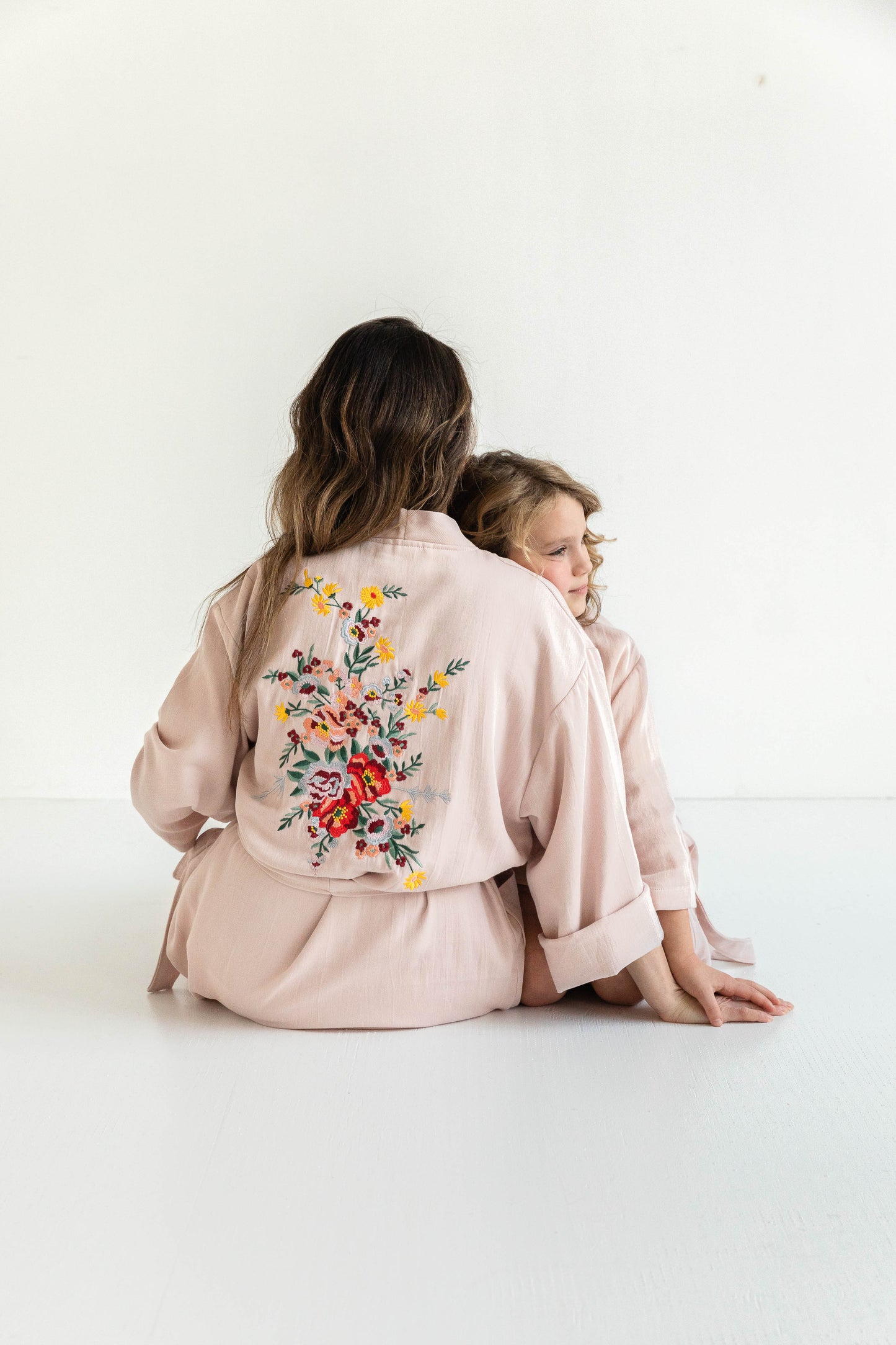 Woman wearing  Hammam34 Pink Floral Embroidered Kimono and  sitting on the floor and her daughter wearing a pink floral embroidered kids kimono sitting with her